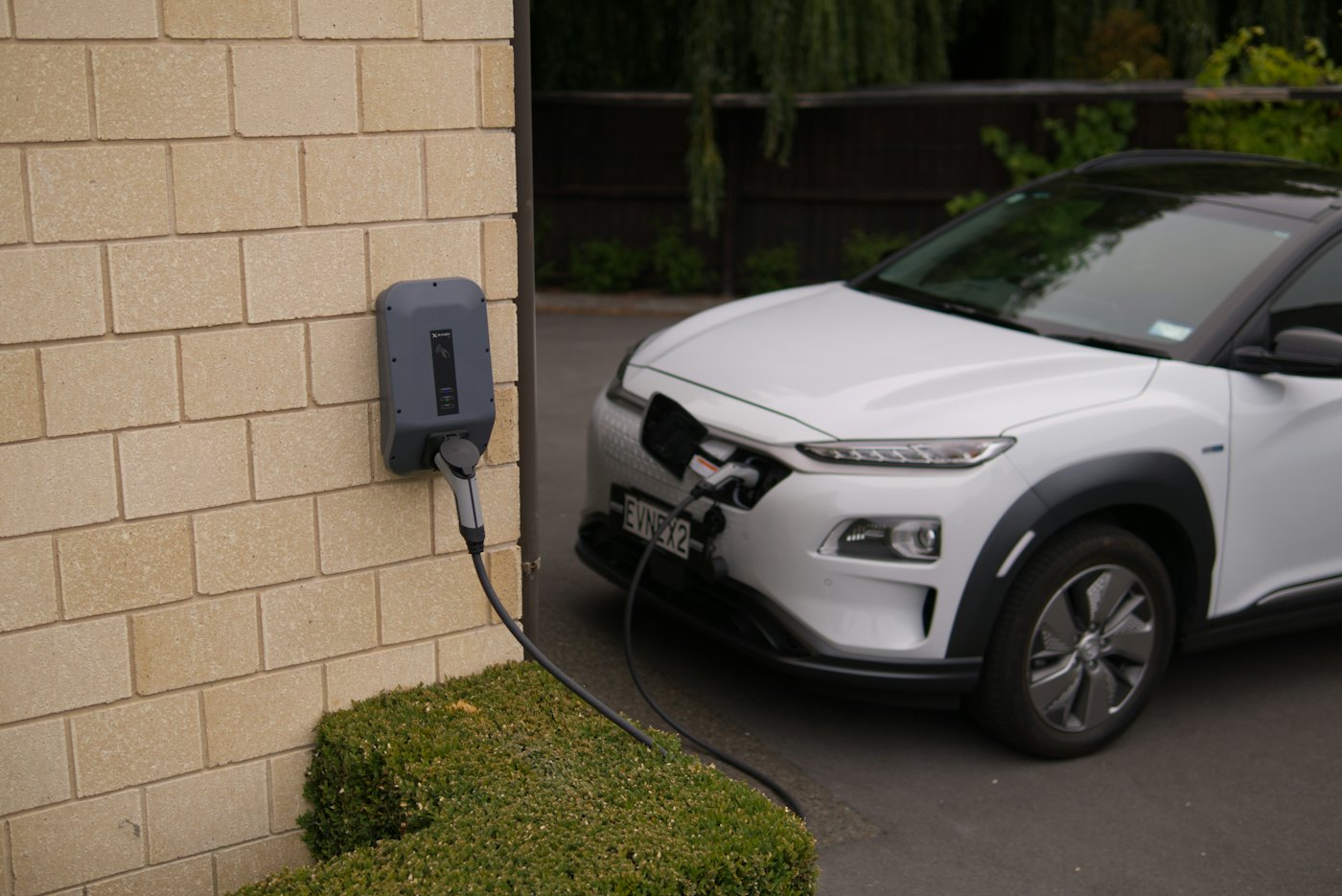 An electric car charging at a wall charger outside a brick house