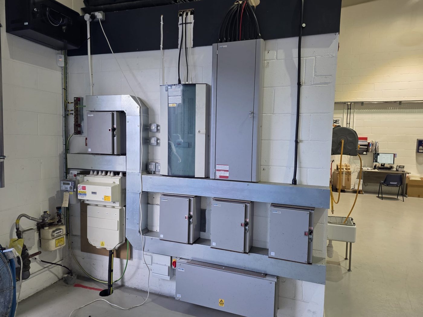 A complete intake and distribution wall: main switchgear, metering and three-phase boards linked with galvanised trunking
