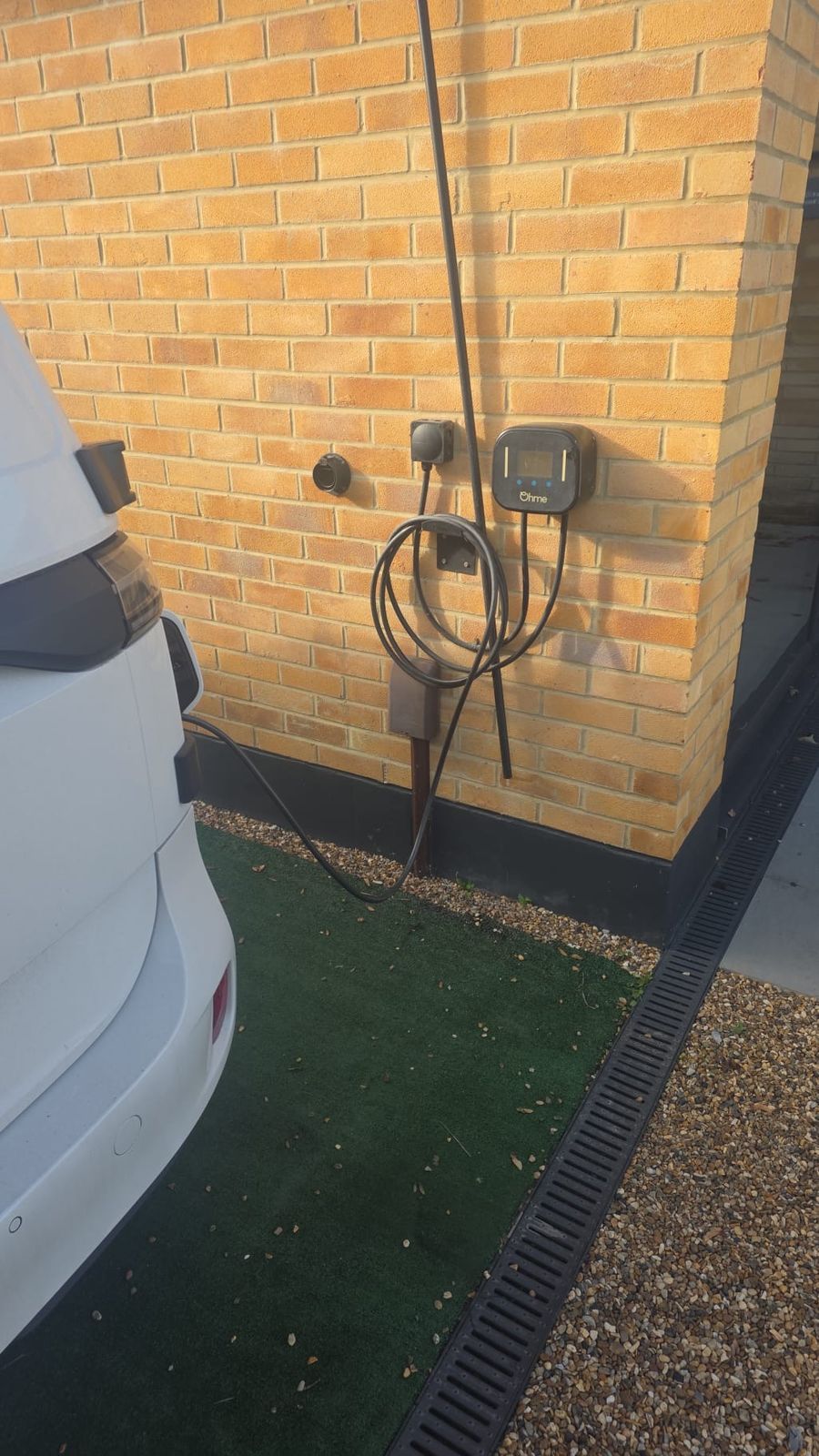 An Ohme smart charger mounted on the side wall, with the tethered cable stowed on its holder