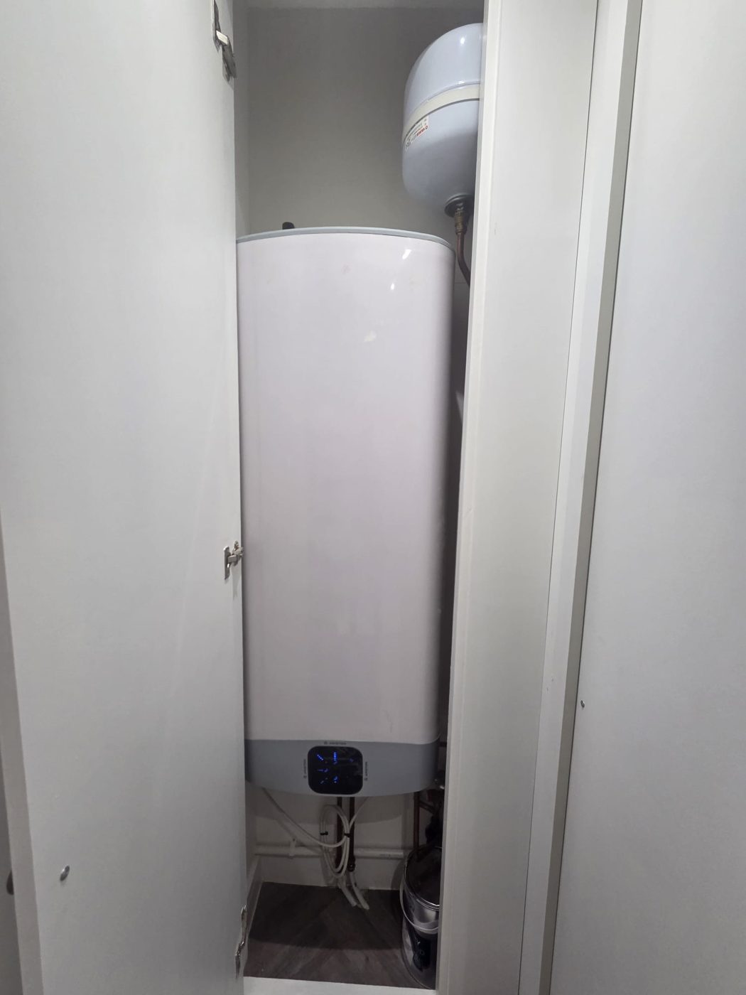 A slimline electric water heater with its expansion vessel, neatly fitted in a cupboard with a digital control panel